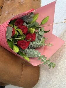 A bouquet of red roses and greenery is placed in a pink paper bag.