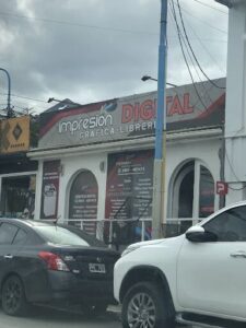 A car is parked in front of a building with a sign that says "Impresion Digital."