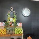 A clock is mounted on a wall next to a potted plant with a birdhouse on top.