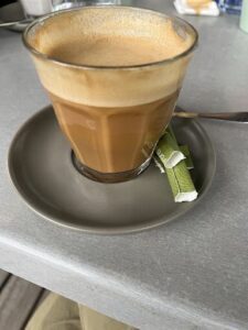 A cup of coffee with a green tea bag in it.