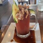 A glass of red liquid with a slice of lime and a shrimp on top.
