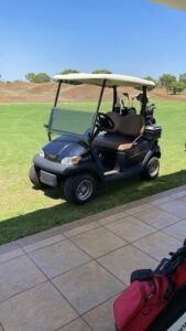 A golf cart is parked on a grassy field, ready for a round of golf.