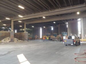 A group of construction workers are standing in a parking lot, surrounded by various construction vehicles.