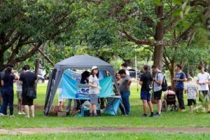 A group of people are gathered around a Pokemon table, with some of them looking at their cell phones.