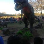 A large dinosaur statue is on display, with a crowd of people gathered around it.