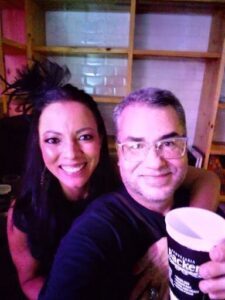A man and woman pose for a picture, both holding a cup.