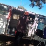 A man is standing in the back of a white van, holding a cat in his arms.