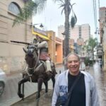 A man poses in front of a statue of a man on a horse, with a bag on his shoulder.