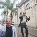A man poses in front of a statue of a man singing.