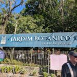 A man stands in front of a sign for the Jardim Botânico do Rio de Janeiro.