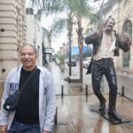 A man stands in front of a statue of a pirate, smiling and enjoying the moment.