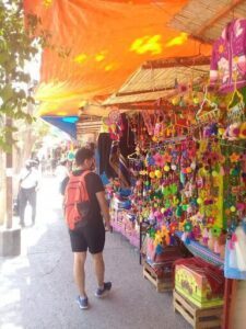 A man wearing a backpack is walking past a colorful market stand.