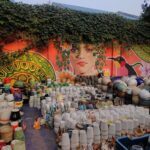 A mural of a woman with a flower in her hair is painted on a wall, surrounded by a variety of vases and pots.