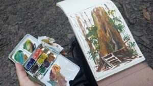 A person is holding a book with a painting of a tree on the cover.