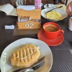 A plate of food sits on a table with a red cup of coffee and a knife.
