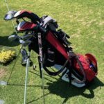 A red golf bag is sitting on the grass, ready for a round of golf.