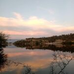 A serene scene of a lake at sunset, with a few boats floating on the water.