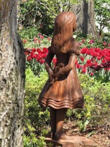 A statue of a girl wearing a dress is standing in a garden.