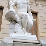 A statue of a man holding a shield is displayed on a pedestal.