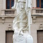 A statue of a woman holding a baby is located in front of a building.