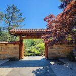 A stone archway leads to a garden filled with greenery and flowers.