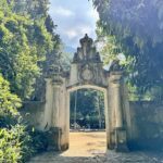 A stone archway with a clock on it, surrounded by trees.