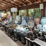 A table full of various pottery items, including vases, bowls, and cups, is displayed in a room with a bamboo ceiling.