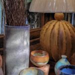A vase of flowers sits on a table next to a lamp and a collection of bowls.