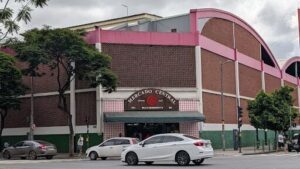 A white car is driving past a building with a pink roof.