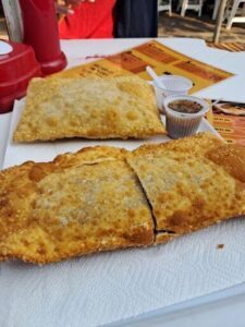 A white plate with two pastries and a cup of sauce.