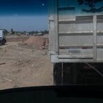 A white semi truck is driving down a road with a construction site in the background.