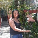 A woman in a black shirt is standing in front of a tree, holding a leaf.