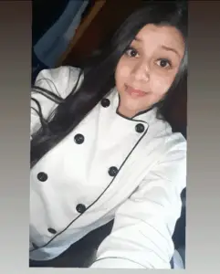 A woman in a white chef's jacket is taking a selfie.