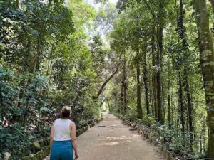 A woman in a white tank top walks down a path in the woods.
