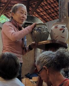 A woman is holding a large vase in front of a group of people.