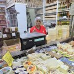 A woman is standing behind a deli counter, smiling and ready to serve customers.