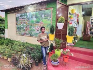 A woman poses in front of a garden with a variety of potted plants.