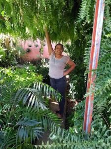 A woman stands in a garden, surrounded by greenery and plants.