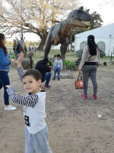 A young boy is posing for a picture in front of a large dinosaur statue.