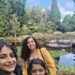 Three women are standing next to a pond, smiling and enjoying their time together.