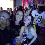 Three women pose for a photo at a party, smiling and holding drinks.