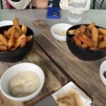 Two bowls of fries are placed on a wooden table, accompanied by a cell phone and a bottle.