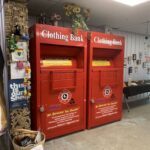 Two red boxes with a yellow sign on them that says "Clothing Bank".