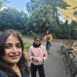 Two women are standing in a park, one of them holding a cell phone.