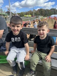 Two young boys sit on a bench, smiling and enjoying their time at the fair.